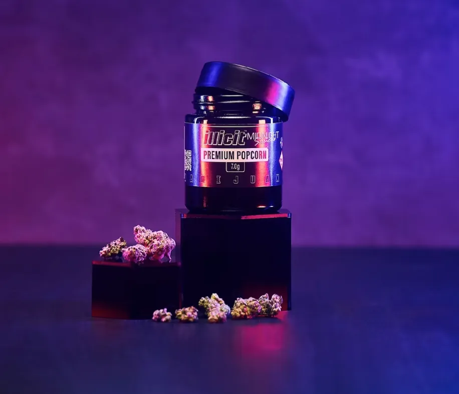 Purple-lit cannabis product display featuring illuminated jar and scattered flower buds on dark surface